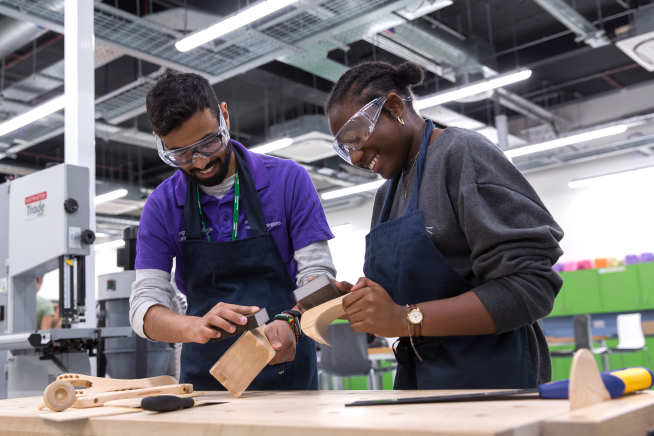 Two people sanding wood at a workbench in the Invention Rooms