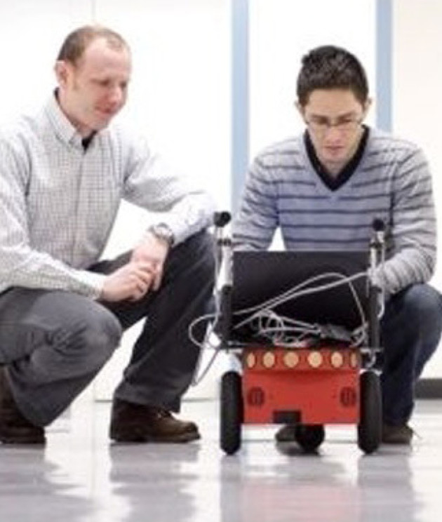 Davison and another man crouching looking at a robot