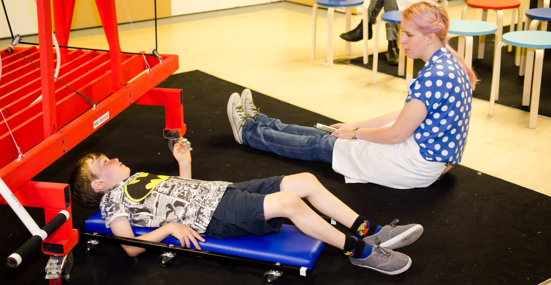 Child uses creeper board to roll under machine