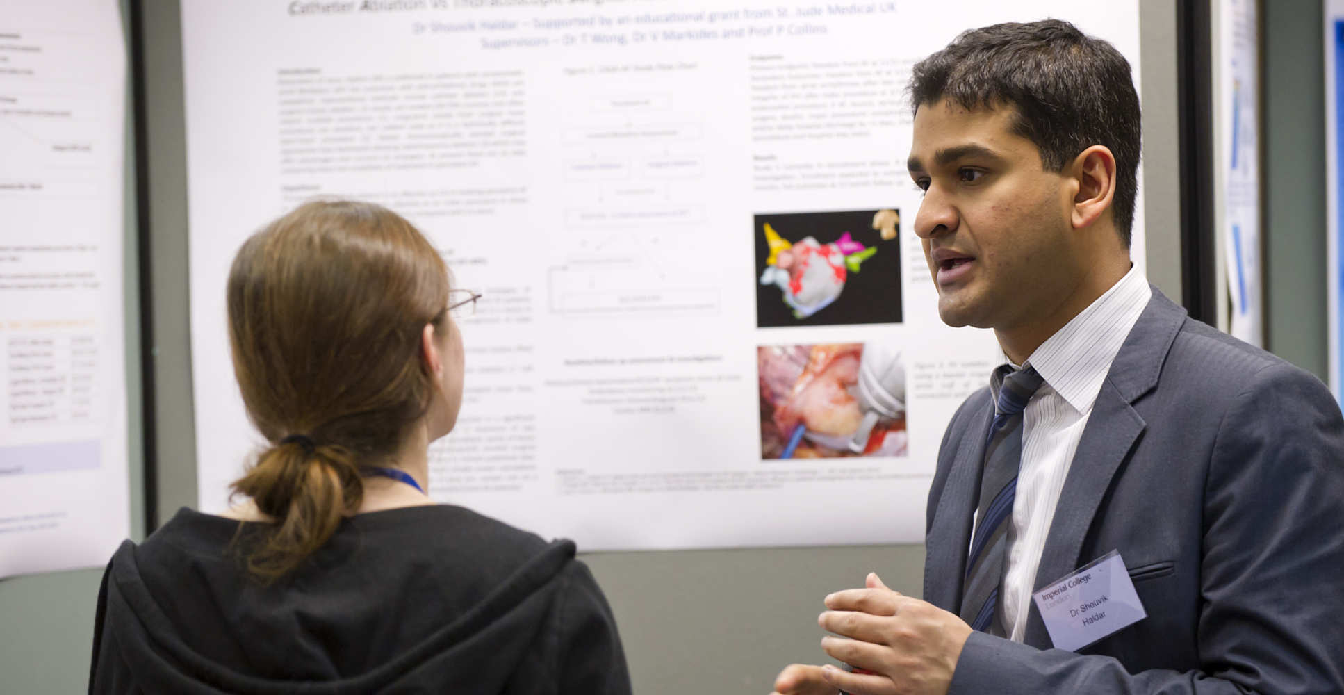 Two people talk in front of poster