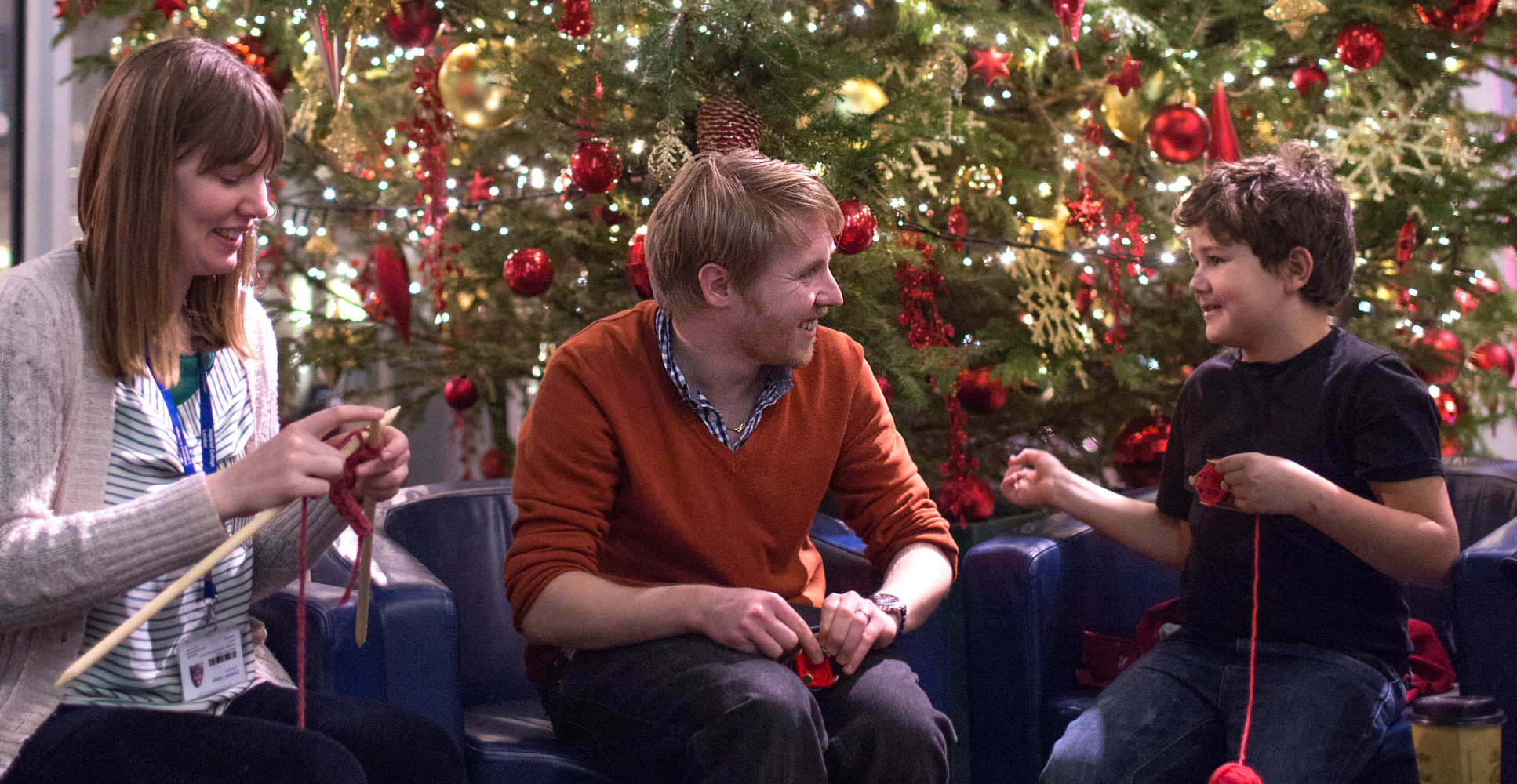 Two adults and child knit in front of xmas tree