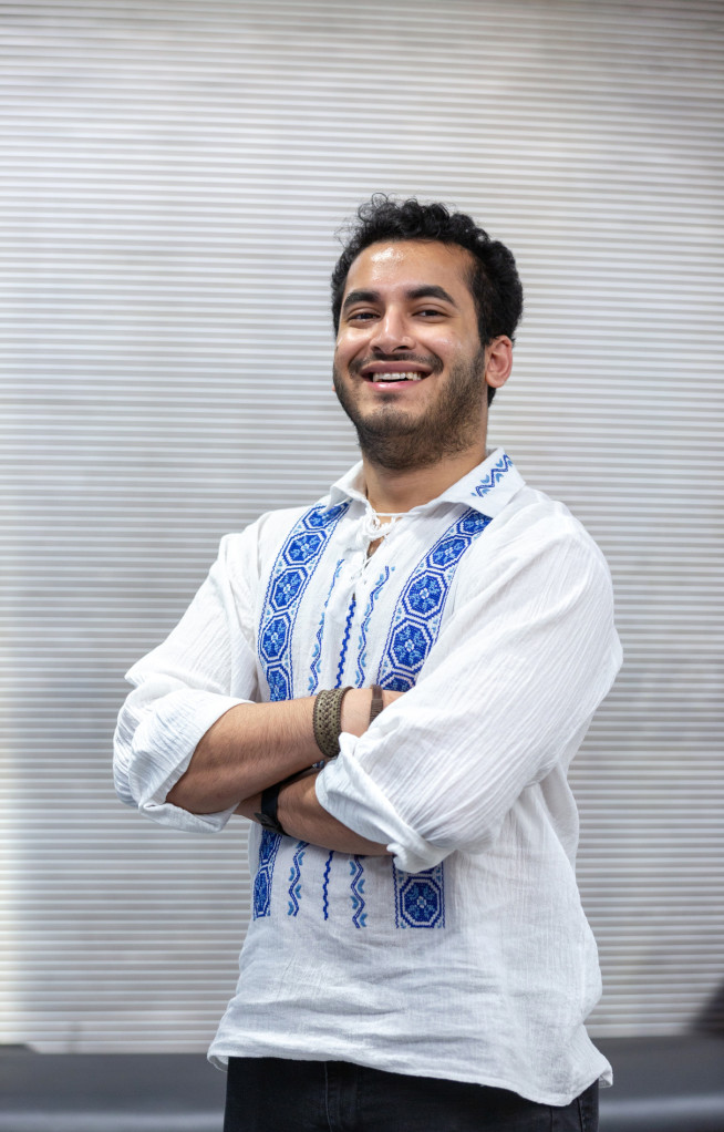 Student smiles at the camera with his arms crossed