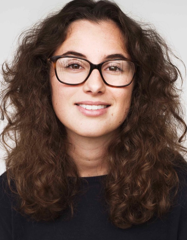 Head-shot of Sigourney Luz, a white woman in her late twenties with long dark curly hair and a big smile.